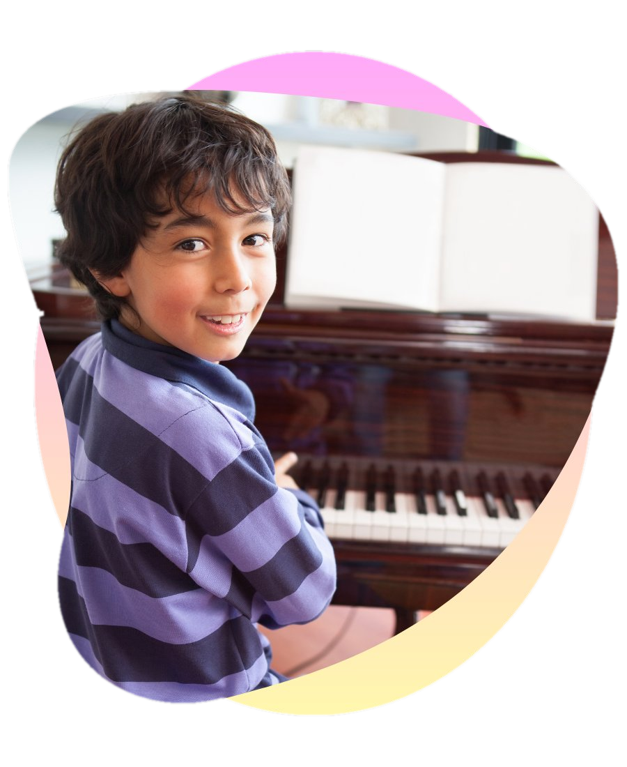 A smiling boy at an upright piano during an in-home lesson with sheet music open